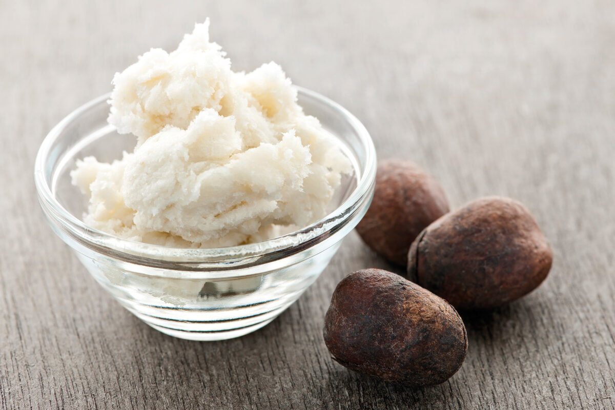 Raw shea butter in a glass bowl beside whole shea nuts